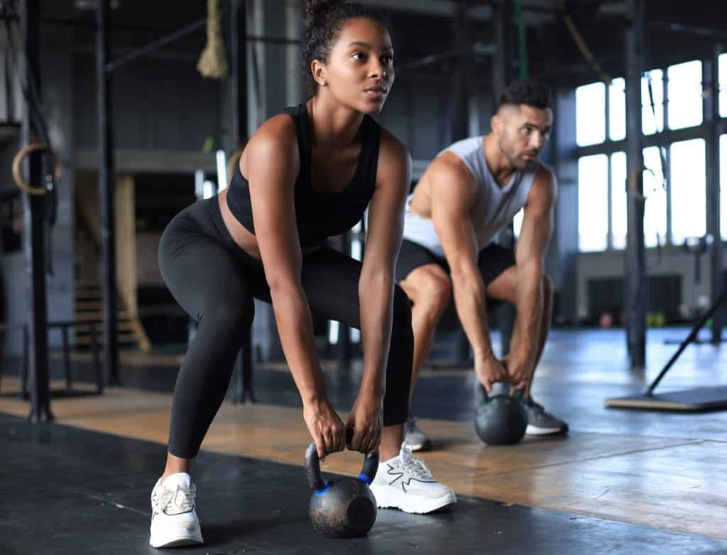 Woman and man in a gym lifting kettle bells for a workout